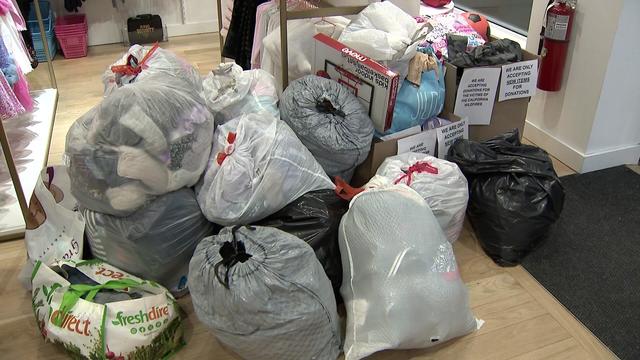 Multiple garbage bags and cardboard boxes filled with clothing sit on the floor of a store.
