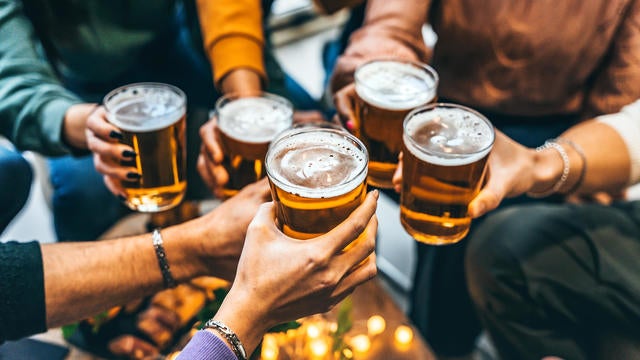 Group of friends drinking and toasting glass of beer at brewery pub restaurant- Happy multiracial people enjoying happy hour with pint sitting at bar table- Youth Food and beverage lifestyle concept