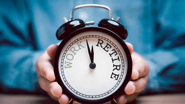 Businessman holding black alarm clock with clockwise countdown from work to retirement.